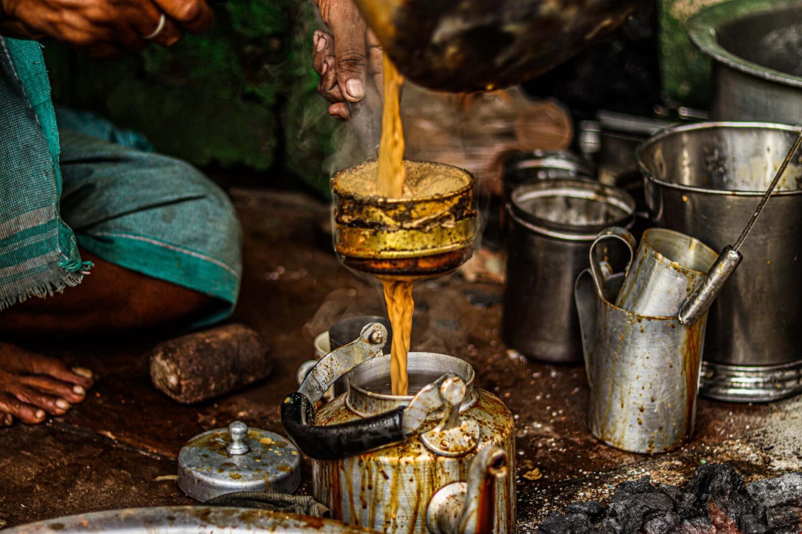 A person pouring oil into an old tea pot.